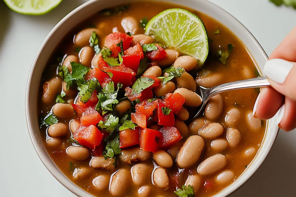 A bowl of finished Crock Pot Pinto Beans garnished with lime and tomato