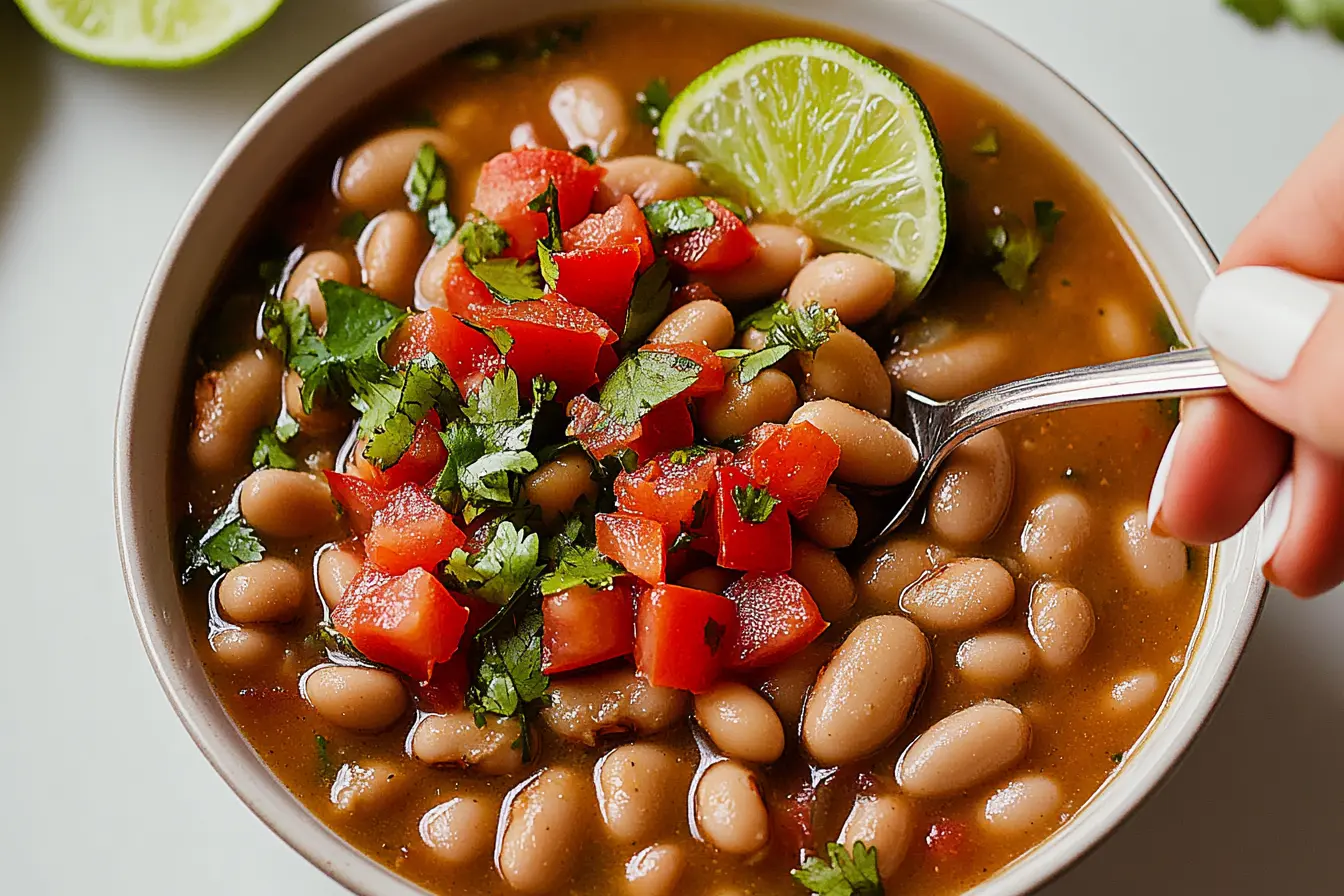 A bowl of finished Crock Pot Pinto Beans garnished with lime and tomato